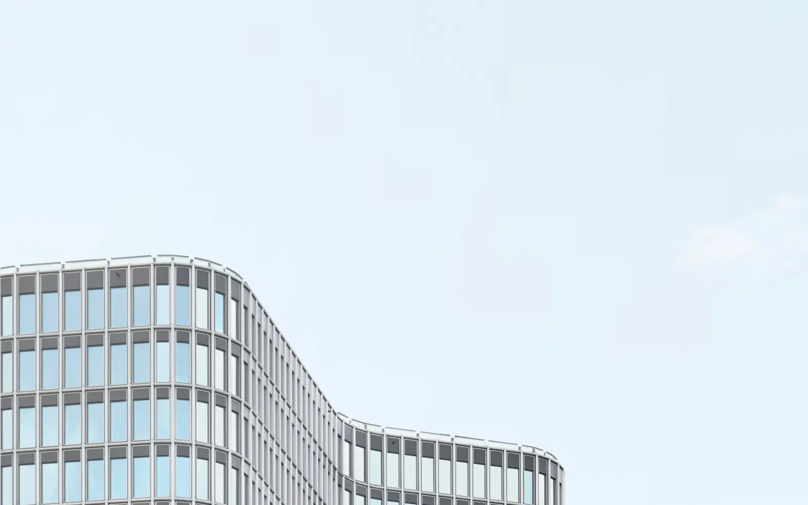 A curved grid of glass windows beneath a dusty blue sky