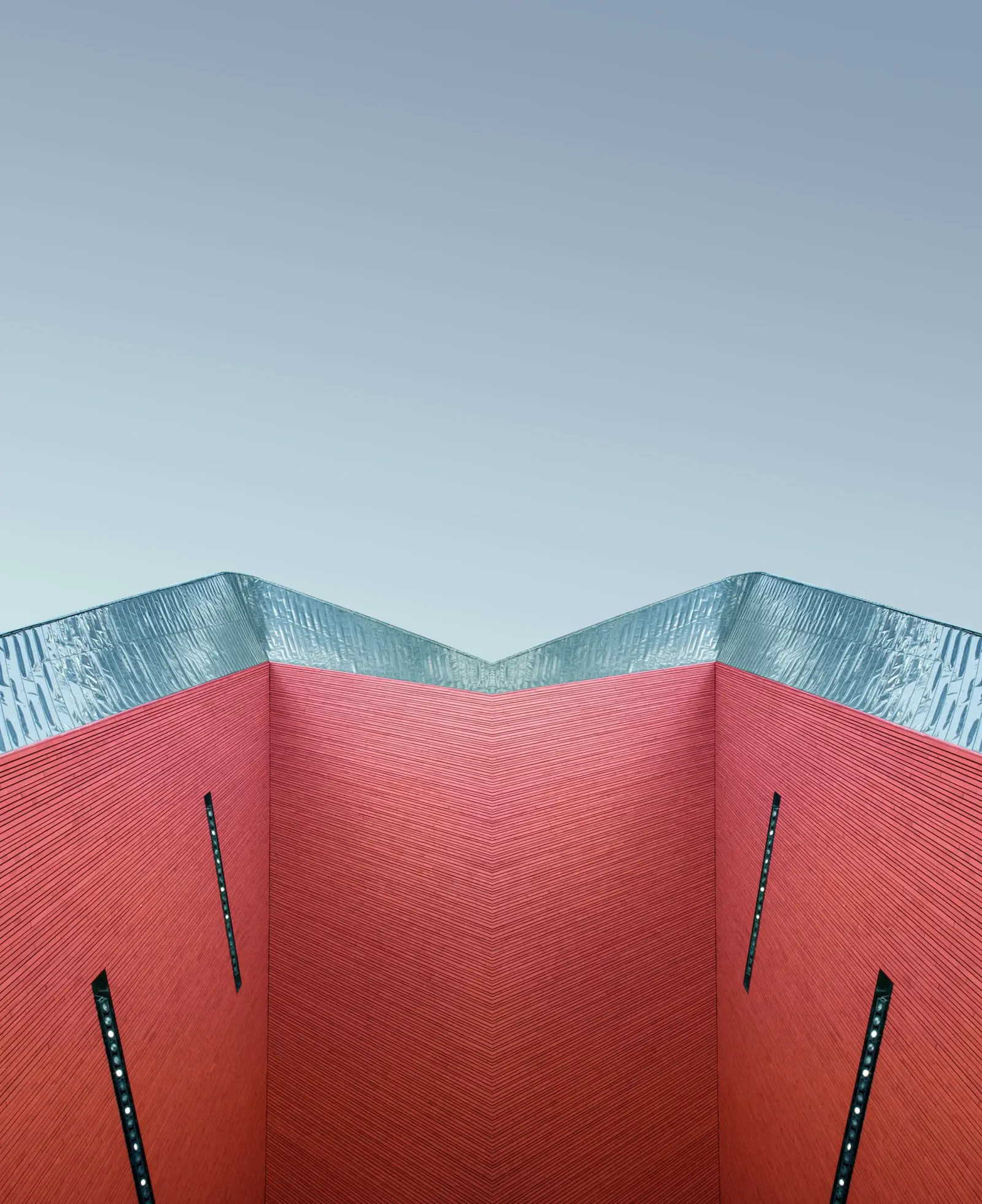 A red geometric facade beneath a pale blue sky